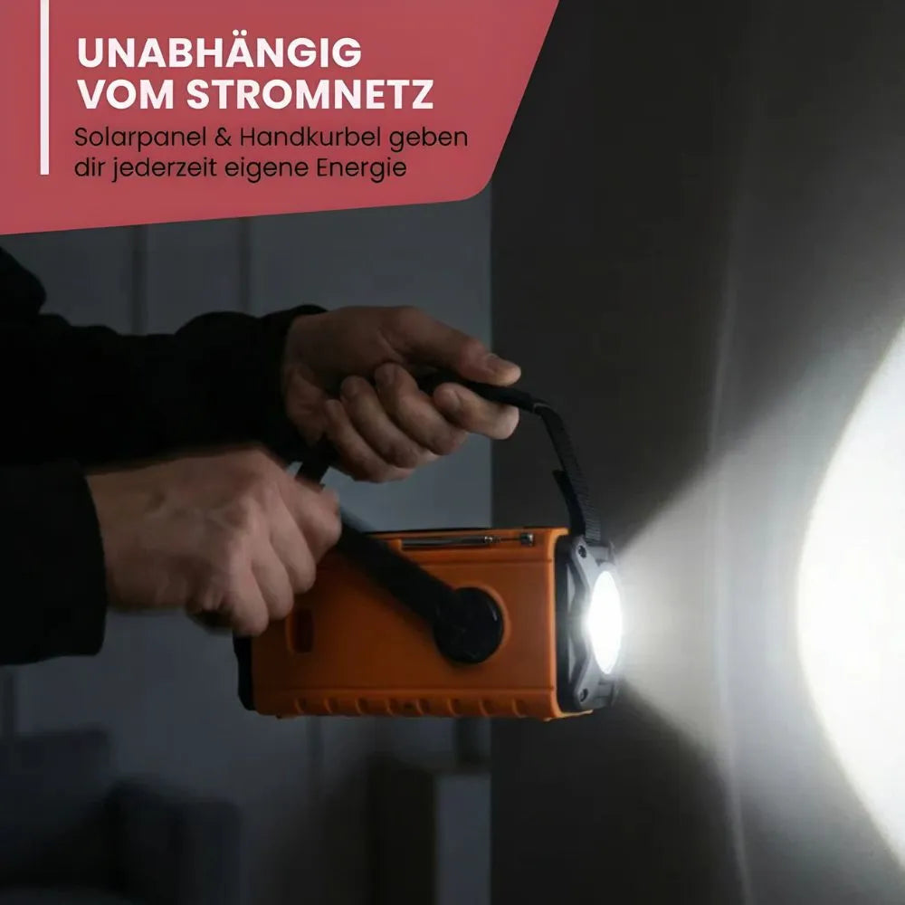 Hände kurbeln am orangen Kurbelradio, die Taschenlampe leuchtet an eine Wand
